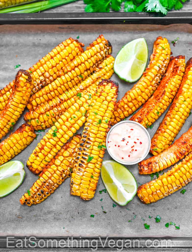 Corn Ribs with lime wedges and dipping sauce on a baking sheet, sprinkled with cilantro