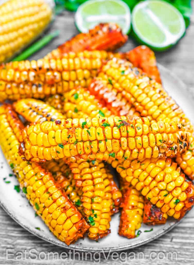 Corn Ribs on a plate, garnished with fresh herbs and served with lime.