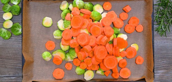 Carrots and Brussels sprouts arranged on a parchment-lined baking sheet