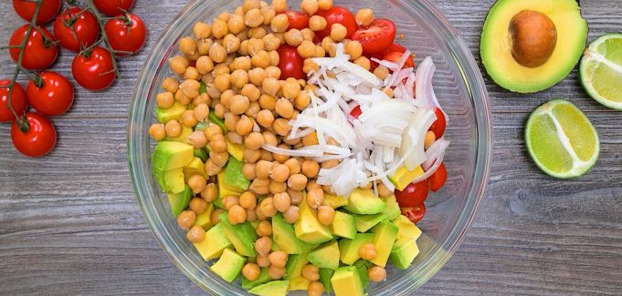 Chickpeas, avocado, cherry tomatoes, cucumbers, and sliced onion in a bowl