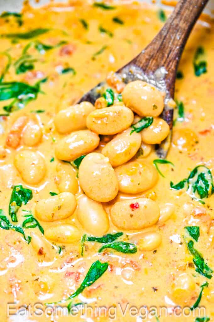 Creamy tomato white beans on a wooden spoon