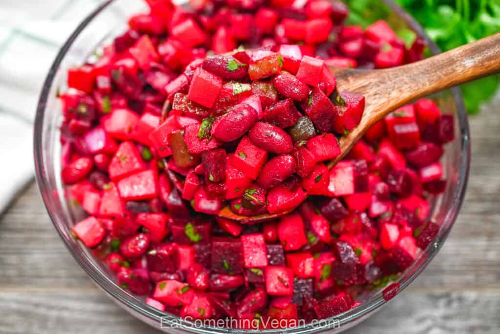 Beet and bean salad in a glass bowl with a wooden spoon