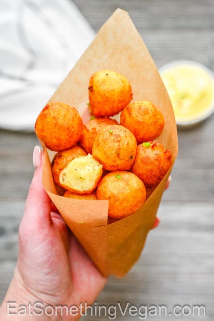 Crispy potato balls served in a paper cone, held by hand