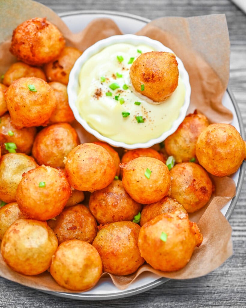 Crispy golden potato balls served with creamy dipping sauce on a parchment-lined plate