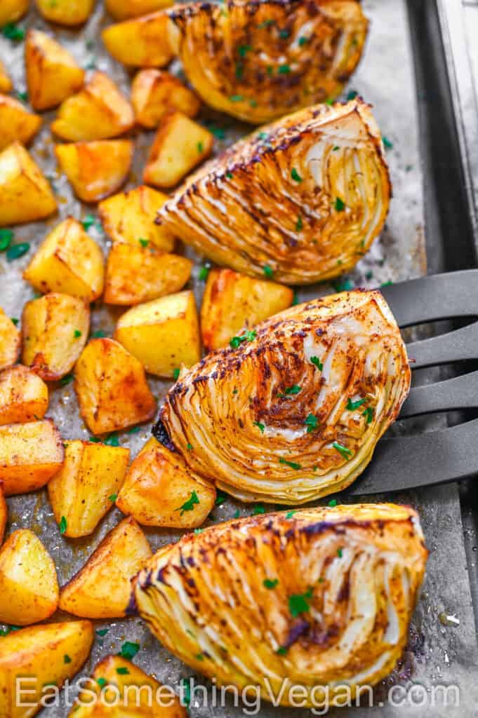 Roasted cabbage wedges and potatoes on a baking sheet with a spatula