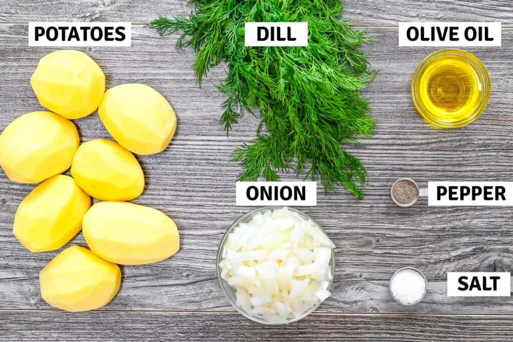 Peeled potatoes, onion, dill, olive oil, salt, and pepper on a table
