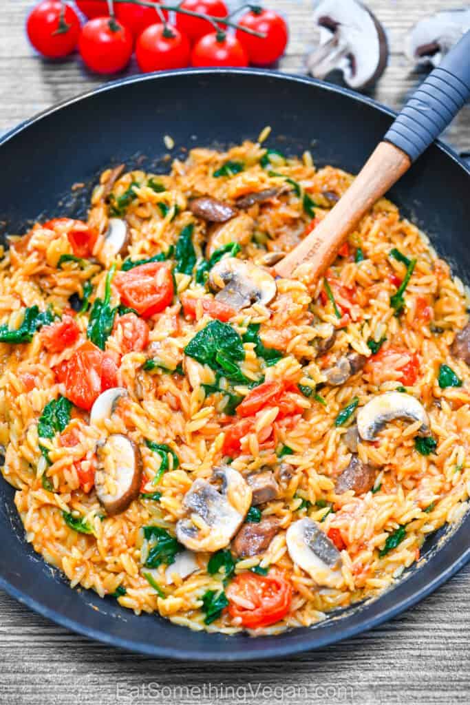 Creamy one-pan orzo with mushrooms, spinach, and cherry tomatoes in a skillet