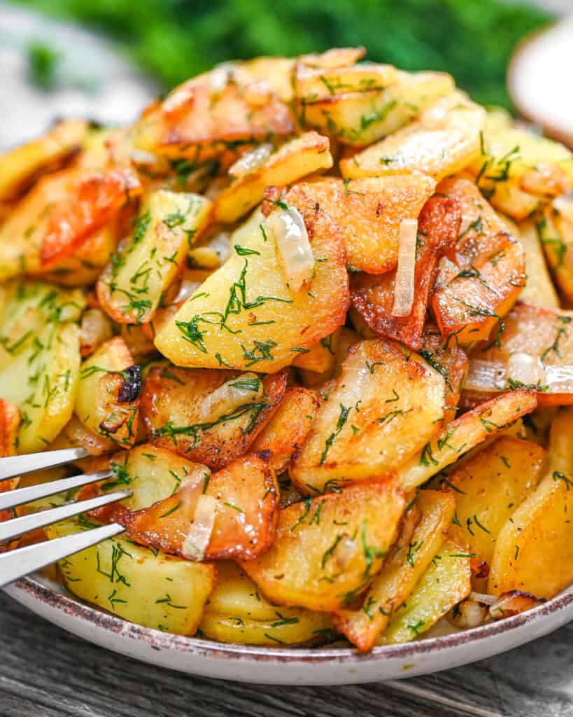 Golden crispy fried potato slices with onion and fresh dill on a plate