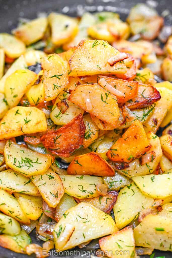 Golden crispy fried potato slices with onion and fresh dill in a skillet