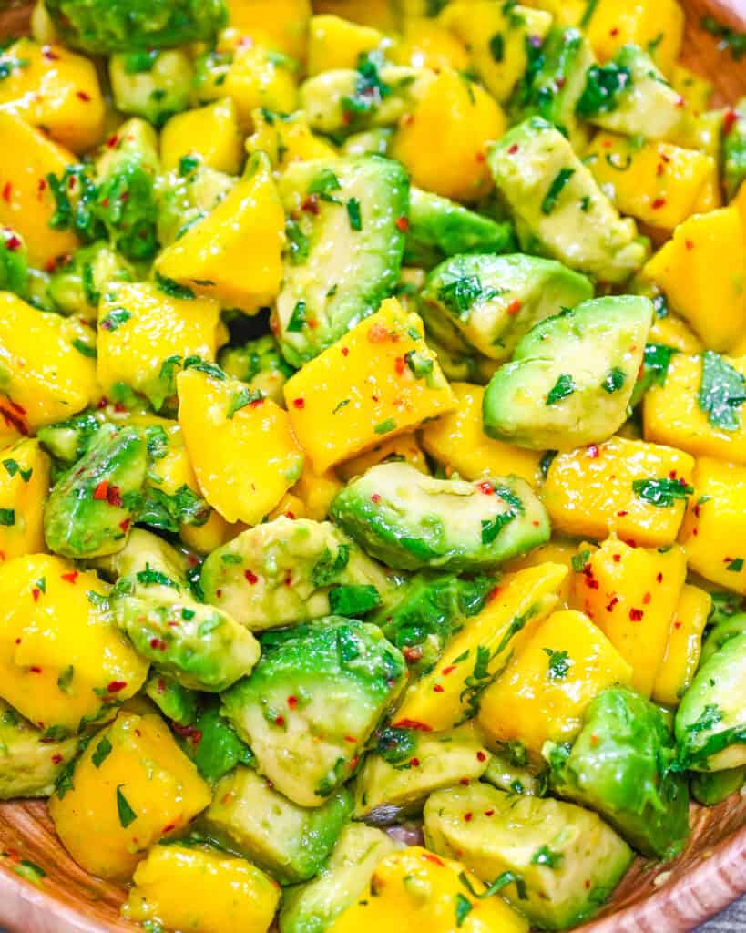 Mango avocado salad with fresh cilantro, lime juice, and red pepper flakes in a wooden bowl, close-up.