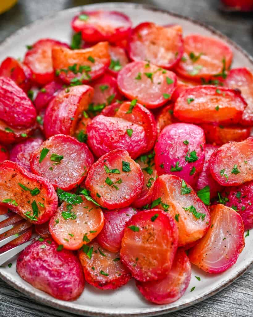 Roasted radishes with golden edges and fresh parsley on a white plate.
