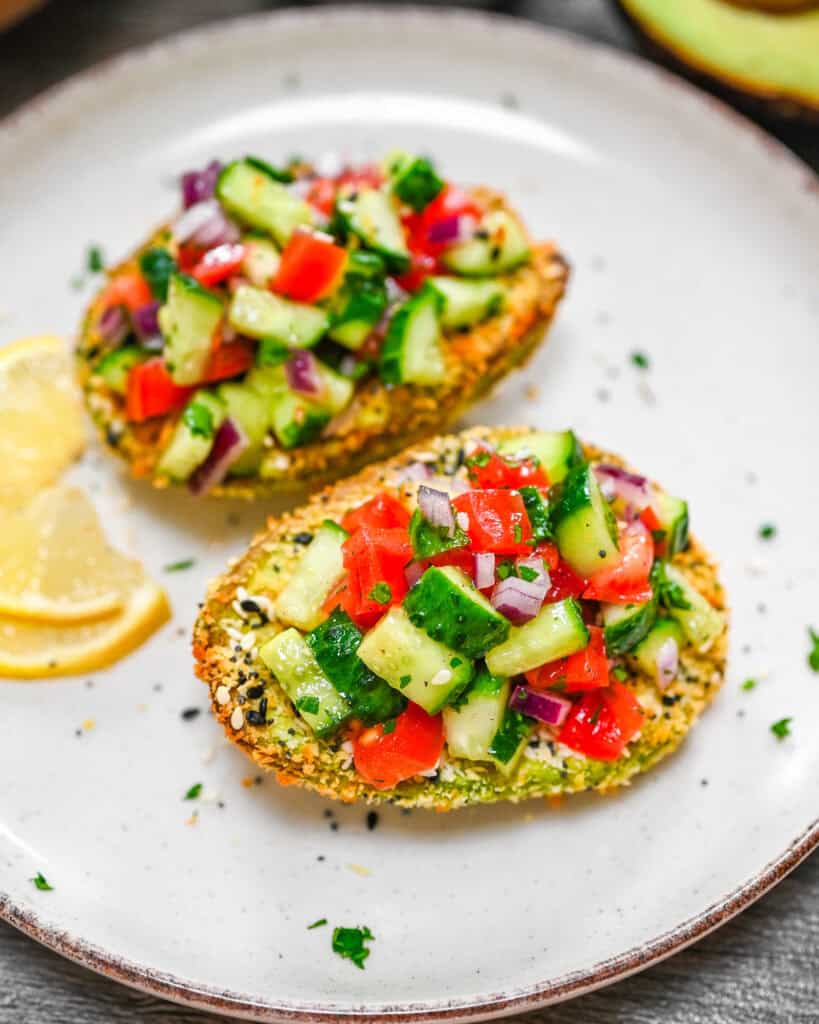Crispy air fryer avocado topped with cucumber tomato salad on a plate