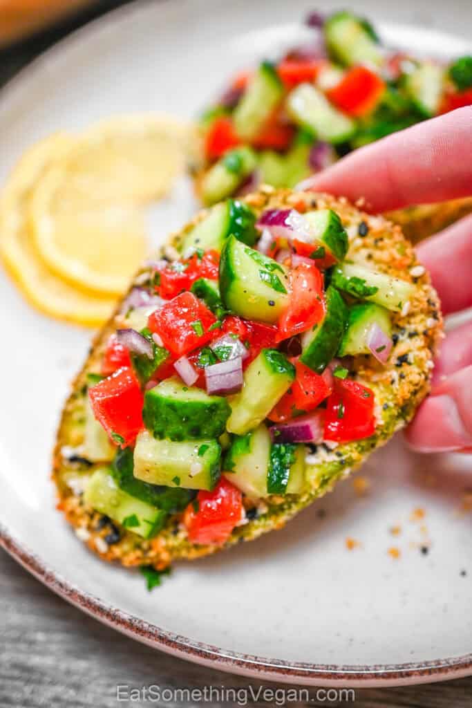 Crispy air fryer avocado topped with cucumber tomato salad in hand