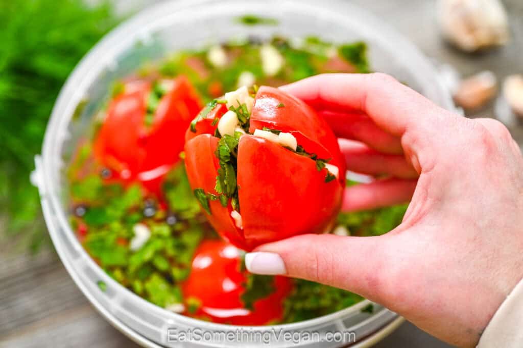 holding a marinated tomato stuffed with garlic and herbs