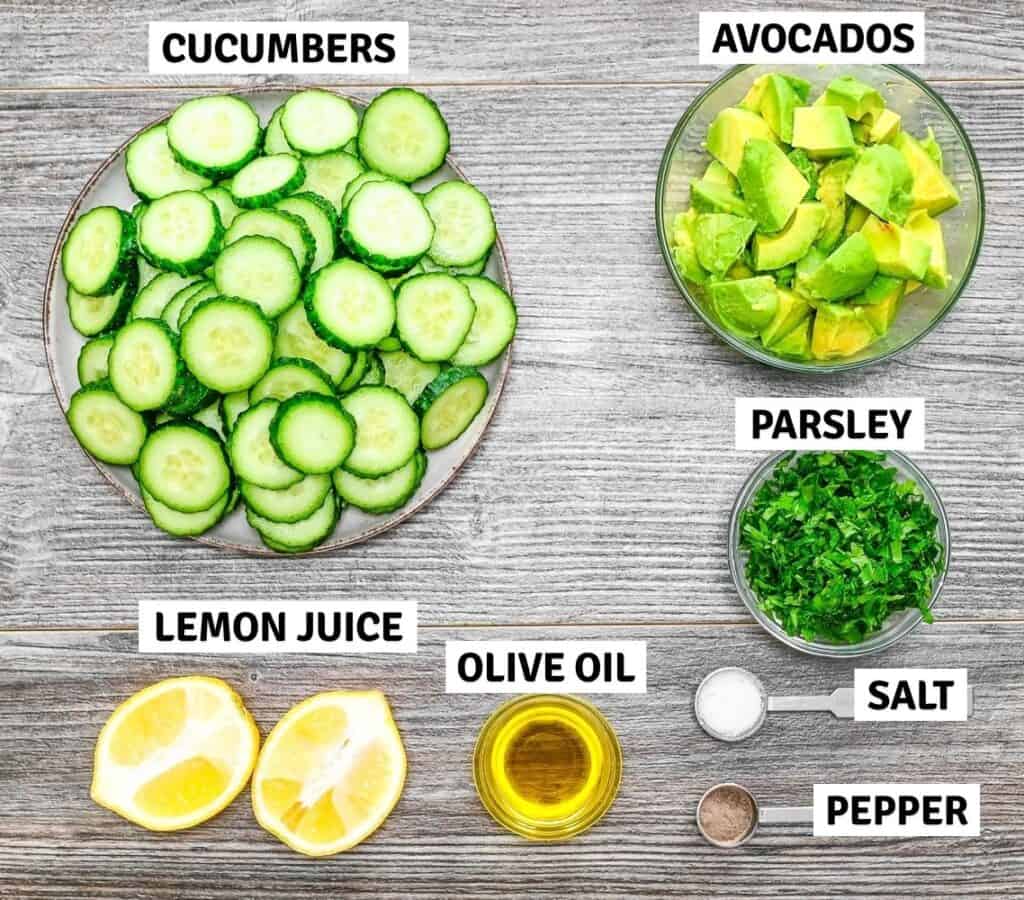 Ingredients on a table including cucumbers, avocado, herbs, lemon, and olive oil