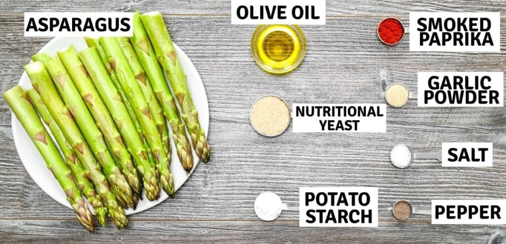 Flat lay of ingredients for smashed asparagus: fresh spears, olive oil, nutritional yeast, potato starch, smoked paprika, garlic powder, salt, and pepper.