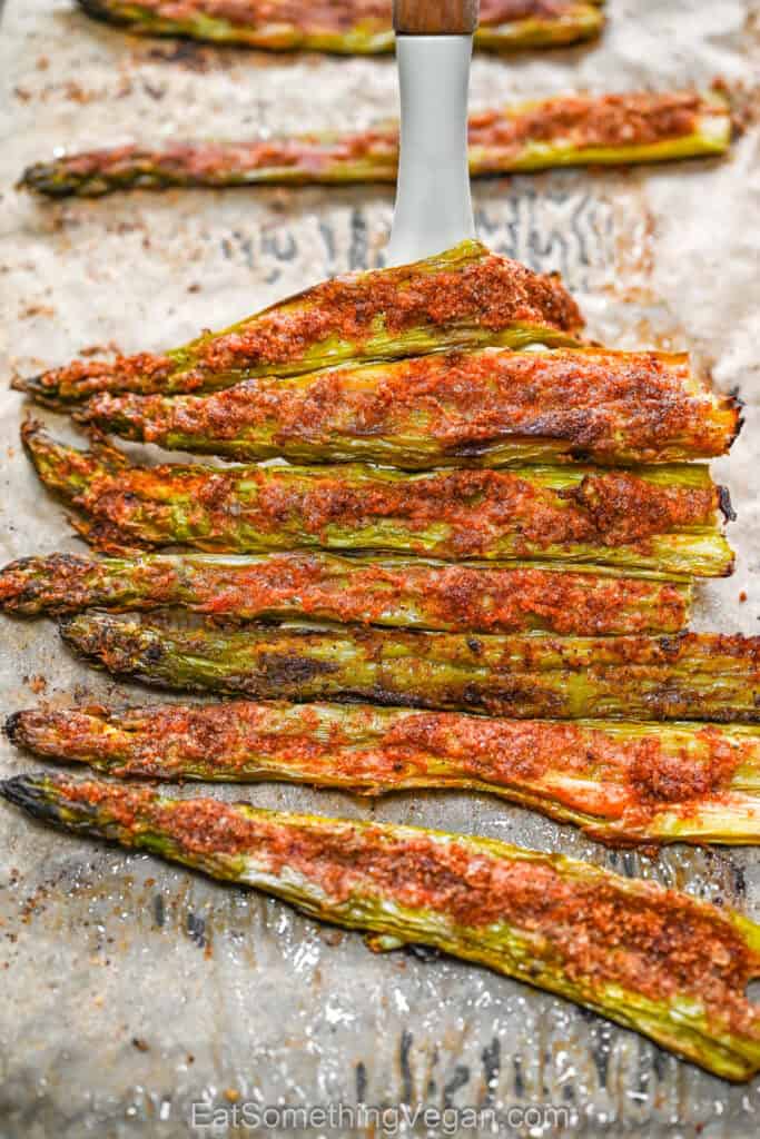 Crispy Smashed Asparagus on a baking sheet being lifted with a spatula.
