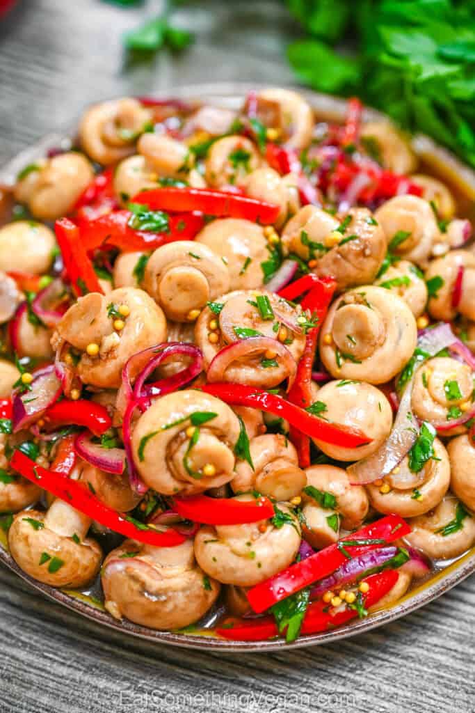 Zesty Garlic Marinated Mushrooms in a bowl with sliced red bell peppers, purple onions, fresh herbs, and mustard seeds.