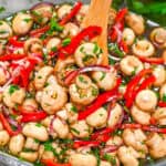 Zesty Garlic Marinated Mushrooms with sliced red bell peppers, purple onions, and fresh herbs being stirred in a glass bowl with a wooden spoon.