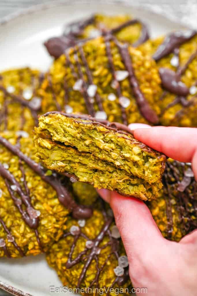 A hand holding a broken matcha coconut cookie, showing its chewy and soft green inside texture.