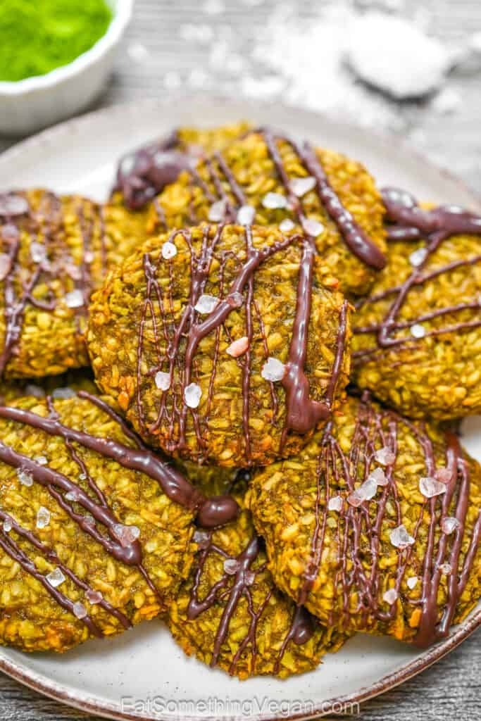 A plate of baked matcha coconut cookies drizzled with melted chocolate and sprinkled with flaky sea salt.