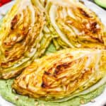A close-up square shot of golden roasted cabbage wedges with crispy charred edges on a bed of green avocado cream, ready to eat.