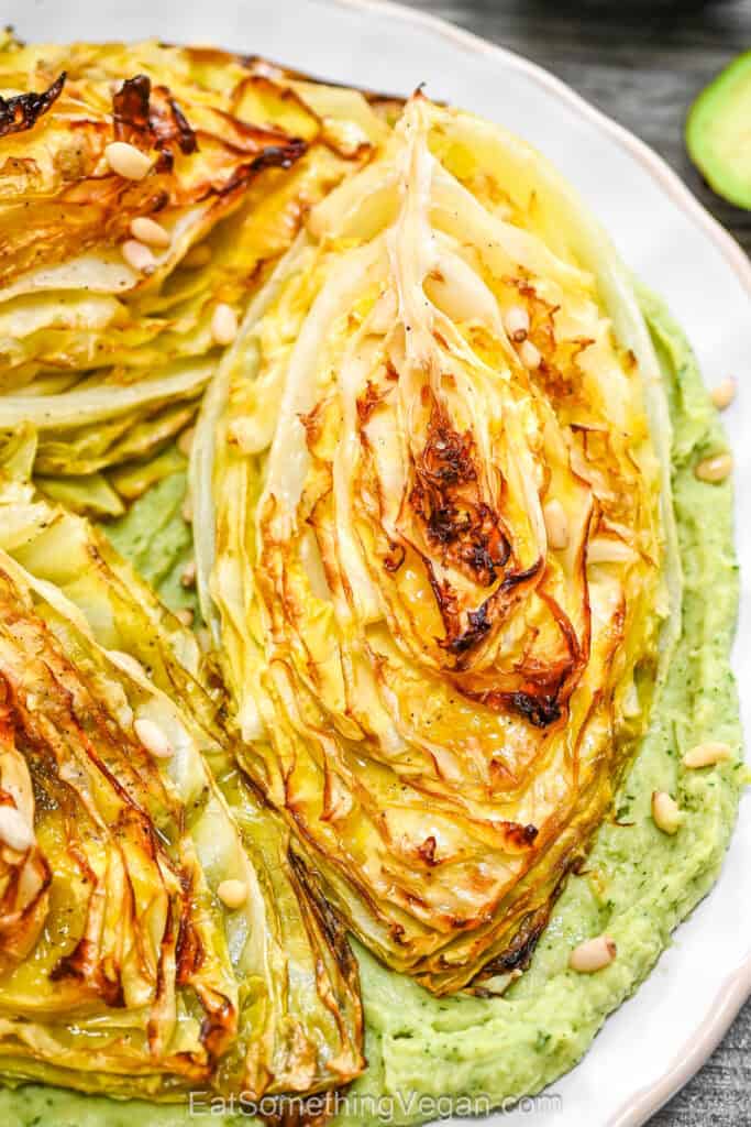 A final serving of crispy roasted cabbage wedges over a smooth green cream base, garnished with toasted pine nuts.