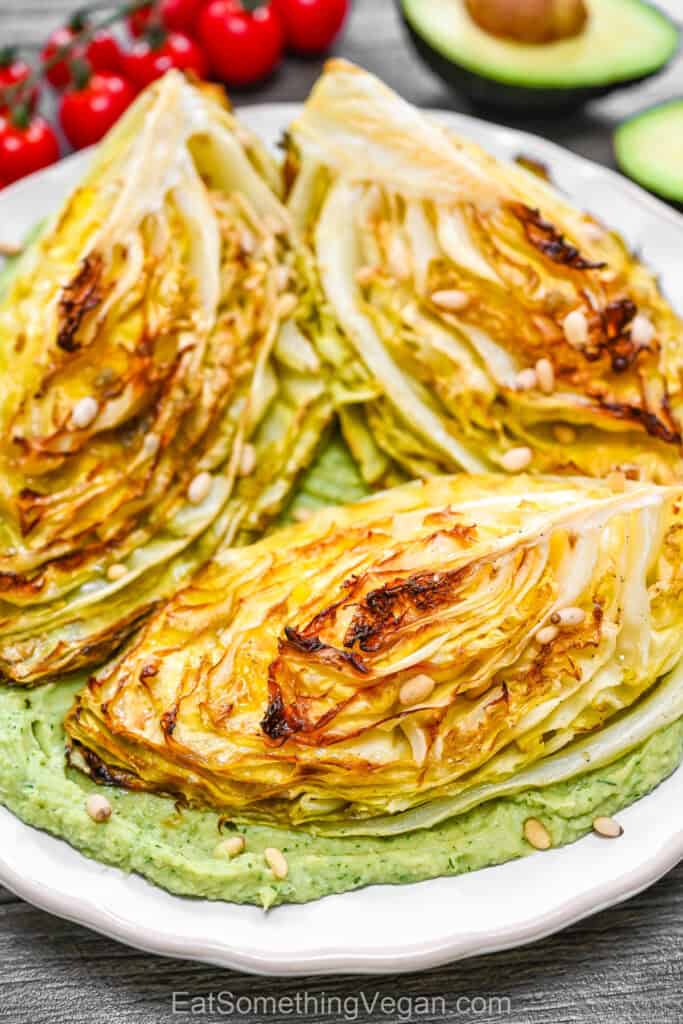 A serving of roasted cabbage wedges with golden charred edges on a bed of green avocado cream, ready to eat.