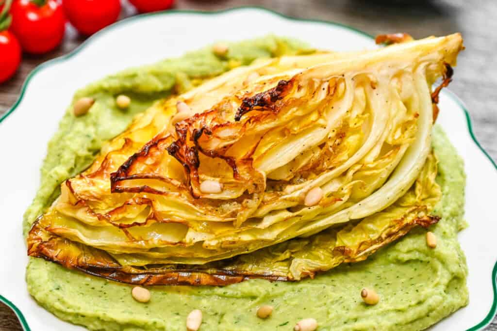 A serving of golden roasted cabbage with crispy charred edges on a bed of smooth avocado cream, ready to eat.