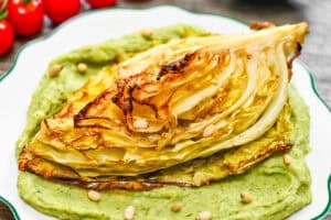 A serving of golden roasted cabbage with crispy charred edges on a bed of smooth avocado cream, ready to eat.