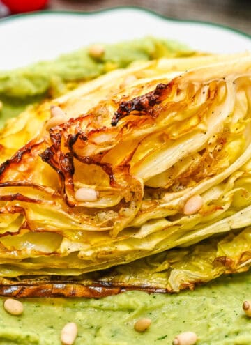 A serving of golden roasted cabbage with crispy charred edges on a bed of smooth avocado cream, ready to eat.