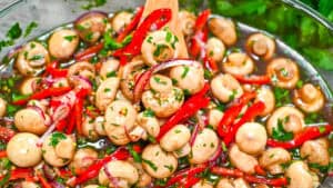 Close-up of marinated whole button mushrooms with bright red bell peppers, purple onions, and fresh herbs in a zesty garlic dressing.