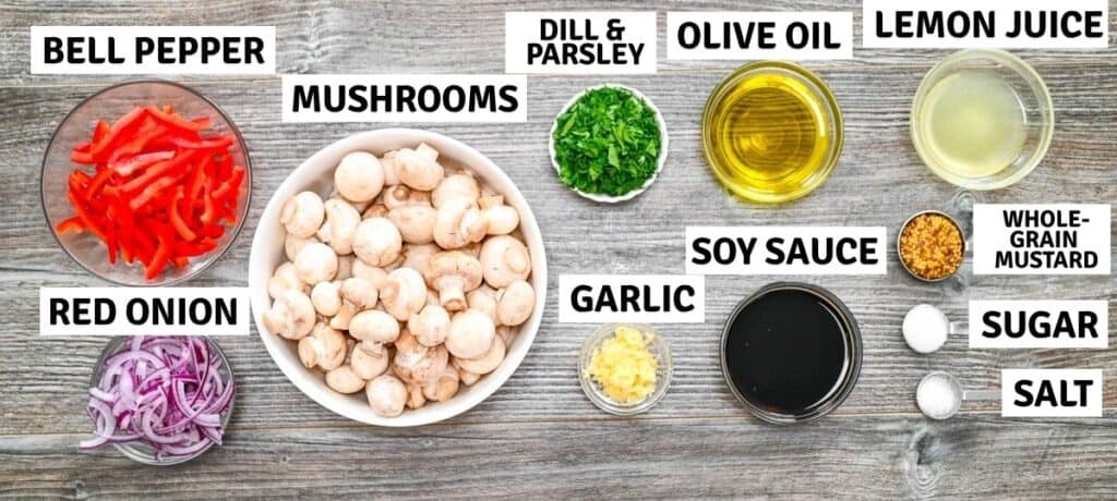 Ingredients for marinated mushrooms arranged on a gray wooden surface, including bowls of mushrooms, red peppers, onions, herbs, and sauces.