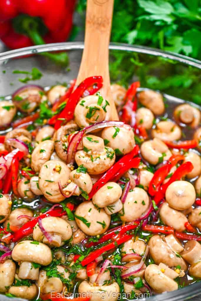 Zesty marinated mushrooms with red peppers, onions, and fresh herbs in a glass bowl.