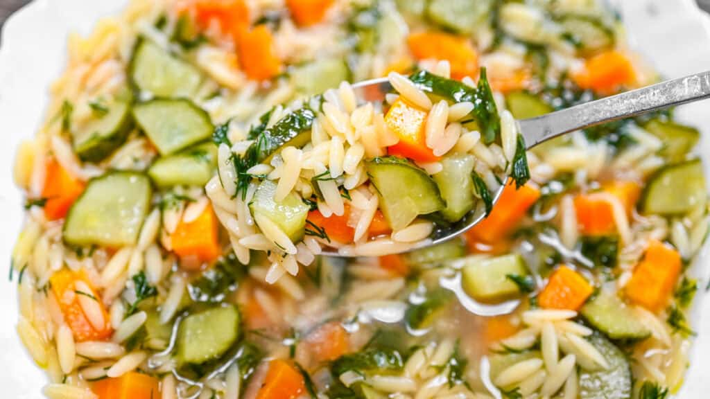 Cucumber Orzo Soup being scooped up with a metal spoon.