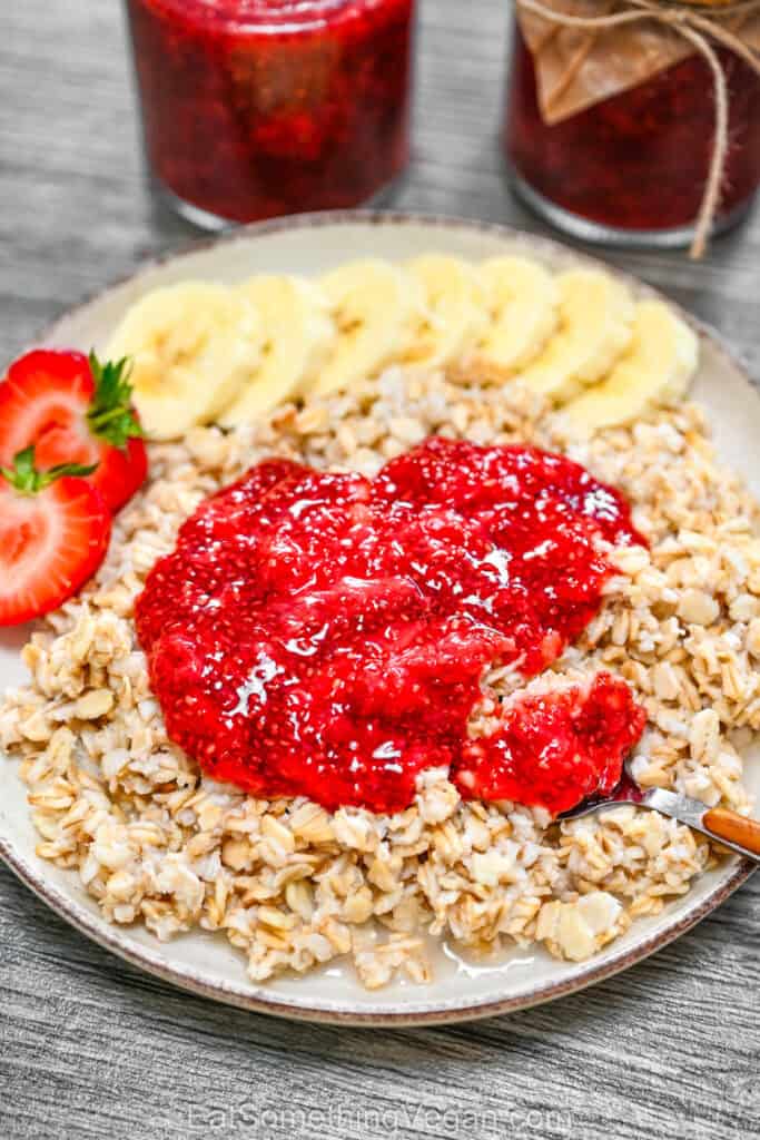 3-Ingredient Strawberry Chia Jam served on top of a bowl of oatmeal, garnished with fresh strawberry slices and banana slices.