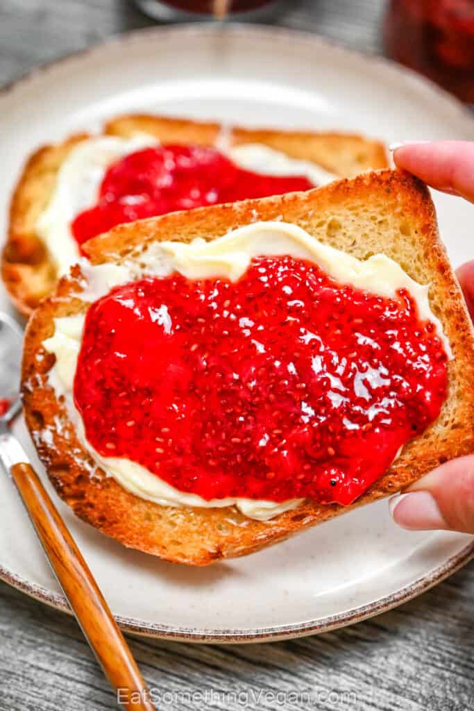 3-Ingredient Strawberry Chia Jam spread over vegan butter on a slice of toasted bread being held by a hand.