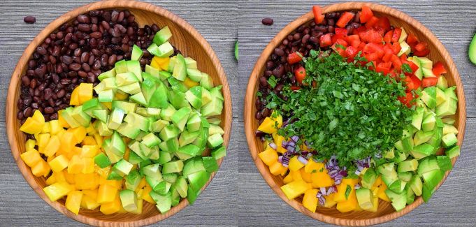 Rinsed black beans, cubed mango, and avocado with chopped cilantro and red pepper in a wooden bowl.