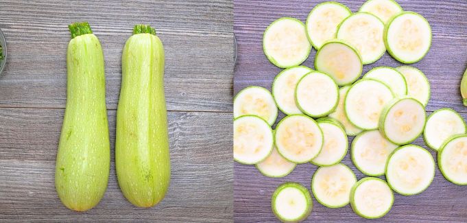 Two whole green zucchinis next to a pile of fresh zucchini slices on a wooden background.