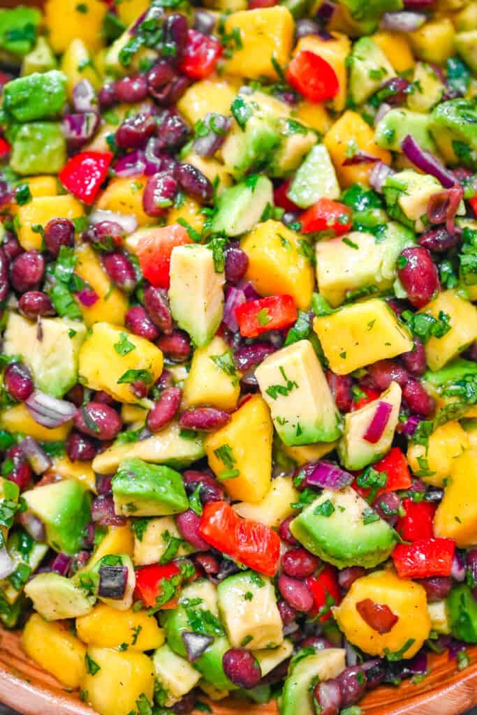 Black bean mango avocado salad with fresh cilantro, lime juice, and red bell pepper in a wooden bowl, close-up.