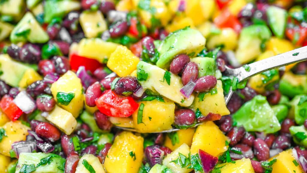 A spoonful of fresh black bean mango avocado salad with chopped cilantro and lime dressing.