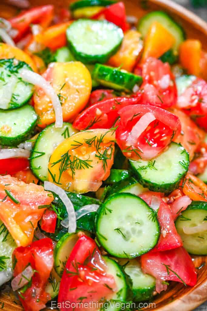 Cucumber Tomato Salad close-up, showing glistening chunks of red and yellow tomatoes, sliced cucumbers, onions, and lots of fresh dill drizzled with olive oil.