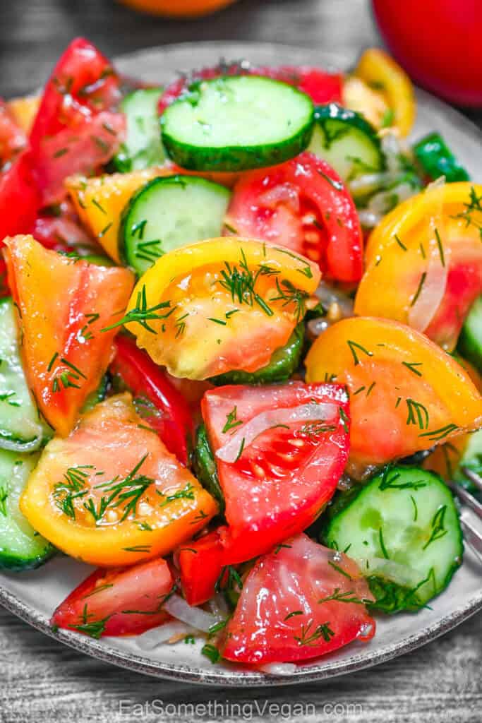 Cucumber Tomato Salad served on a plate, featuring vibrant red and yellow tomatoes, sliced cucumbers, onions, and fresh dill drizzled with olive oil.