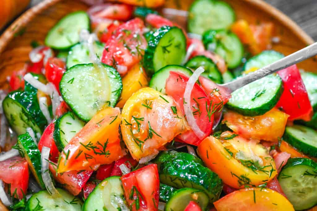 Cucumber Tomato Salad on a spoon, served from a wooden bowl and filled with fresh cucumbers, tomatoes, onions, and dill.