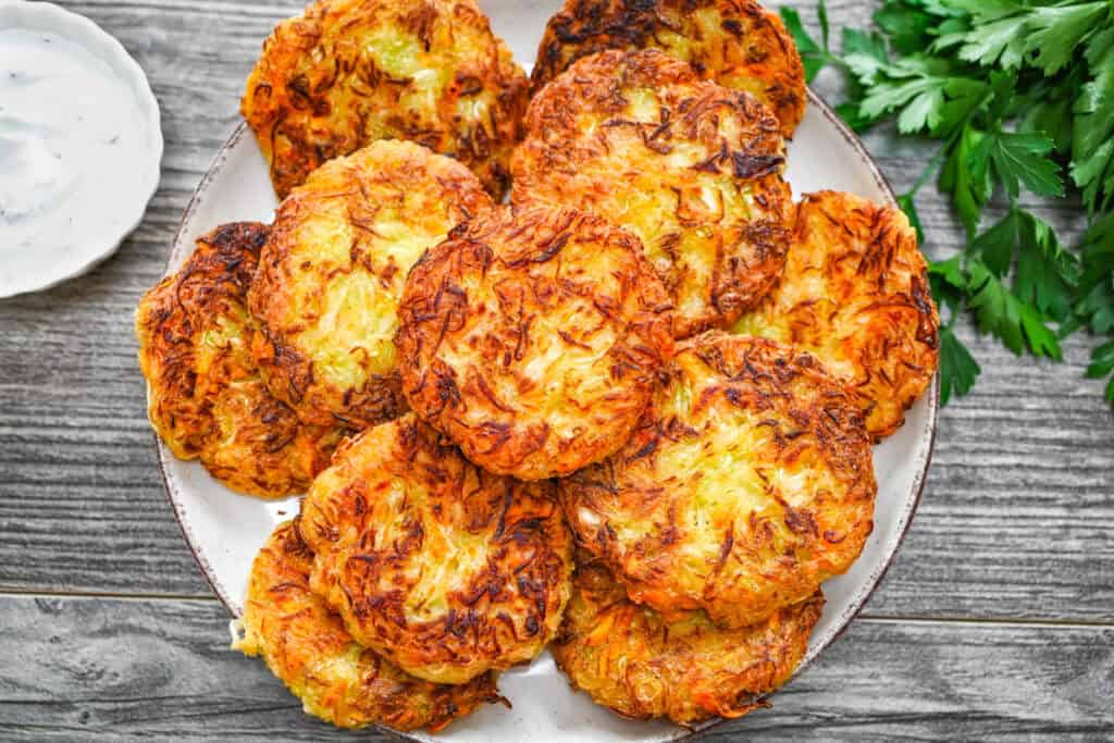 Overhead view of golden crispy cabbage fritters served on a ceramic plate with white sauce and fresh parsley.