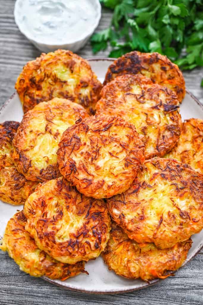Golden crispy cabbage fritters stacked on a plate with dipping sauce and fresh parsley on a wooden table.