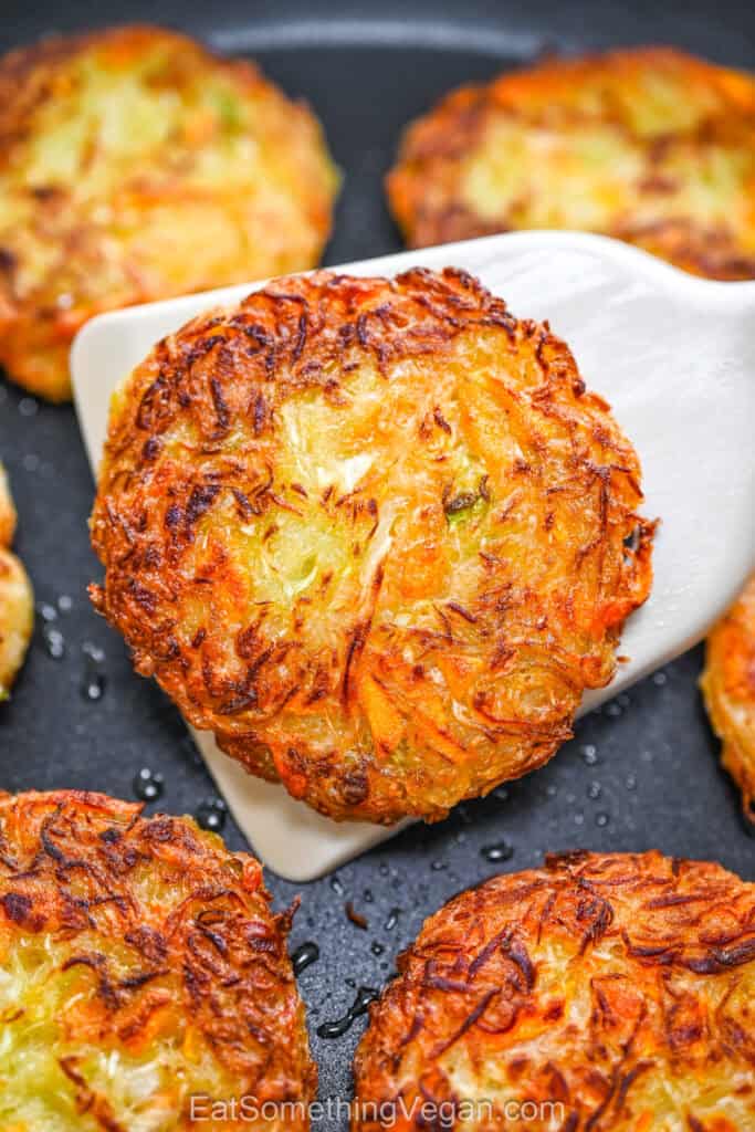 A close-up view of a golden brown, crispy cabbage fritter being lifted with a white spatula in a pan.