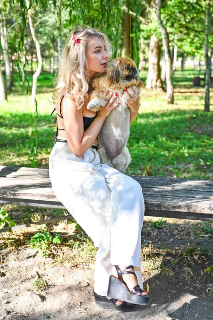 Woman holding her small dog Emma while sitting on a bench in a sunny park.