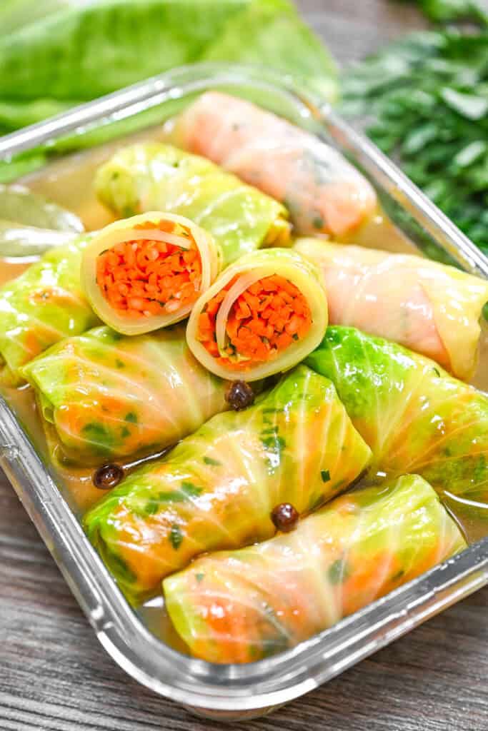 Pickled cabbage rolls stuffed with carrots and herbs in a glass container with pickling brine