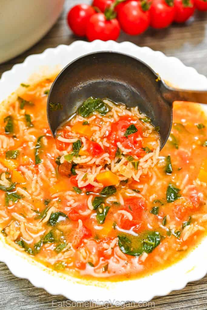 Tomato Spinach Rice Soup, being poured from a ladle into a white bowl.